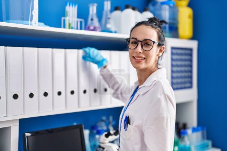 Photo for Young caucasian woman scientist smiling confident holding binder of shelving at laboratory - Royalty Free Image