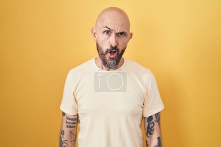 Téléchargez les photos : Homme hispanique avec des tatouages debout sur fond jaune dans le visage de choc, l'air sceptique et sarcastique, surpris avec la bouche ouverte - en image libre de droit