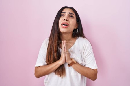 Photo for Young arab woman standing over pink background begging and praying with hands together with hope expression on face very emotional and worried. begging. - Royalty Free Image