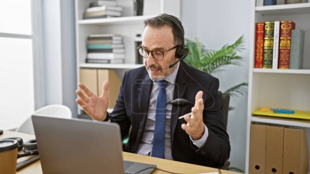 Téléchargez les photos : Malheureux, homme d'âge moyen avec les cheveux gris se disputant sur appel vidéo au bureau tout en travaillant - en image libre de droit