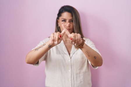 Photo for Blonde woman standing over pink background rejection expression crossing fingers doing negative sign - Royalty Free Image