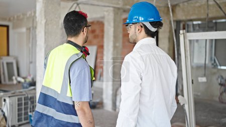 Téléchargez les photos : Deux hommes bâtisseur et architecte debout ensemble vers l'arrière sur le chantier de construction - en image libre de droit