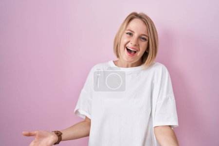 Téléchargez les photos : Jeune femme caucasienne debout sur fond rose souriant gai avec les bras ouverts comme accueil amical, salutations positives et confiantes - en image libre de droit