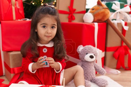 Foto de Adorable chica hispana sentada en el suelo por regalos de Navidad jugando en casa - Imagen libre de derechos
