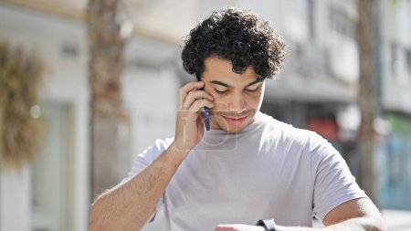 Téléchargez les photos : Jeune homme latin parlant sur smartphone regarder la rue - en image libre de droit