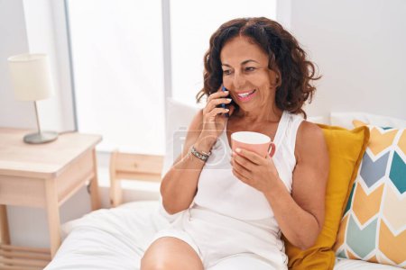 Téléchargez les photos : Middle age woman talking on smartphone drinking coffee at bedroom - en image libre de droit
