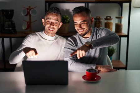 Foto de Pareja homosexual usando ordenador portátil señalando a usted ya la cámara con los dedos, sonriendo positivo y alegre - Imagen libre de derechos