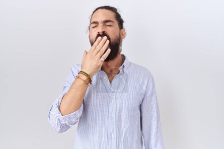 Foto de Hombre hispano con barba vistiendo camisa casual aburrido bostezando cansado cubriendo la boca con la mano. inquietud y somnolencia. - Imagen libre de derechos