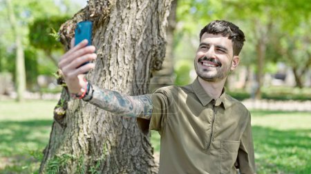 Téléchargez les photos : Jeune homme hispanique souriant confiant faire selfie par le smartphone au parc - en image libre de droit