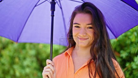 Téléchargez les photos : Jeune belle femme hispanique souriant confiance tenant parapluie au parc - en image libre de droit