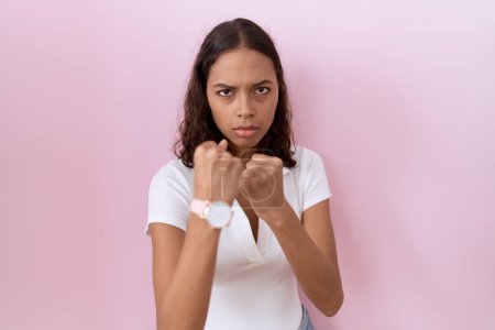 Photo for Young hispanic woman wearing casual white t shirt ready to fight with fist defense gesture, angry and upset face, afraid of problem - Royalty Free Image