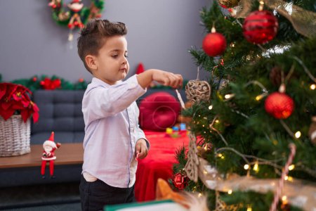 Téléchargez les photos : Adorable bambin hispanique décorant l'arbre de Noël à la maison - en image libre de droit