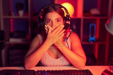 Photo for Young blonde woman playing video games wearing headphones shocked covering mouth with hands for mistake. secret concept. - Royalty Free Image