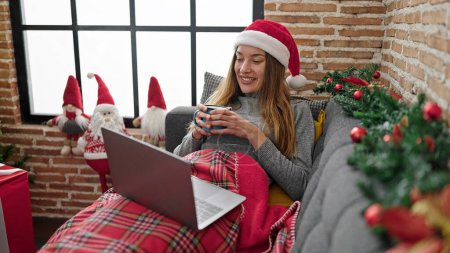 Téléchargez les photos : Jeune femme caucasienne regarder film boire du café célébrant Noël à la maison - en image libre de droit
