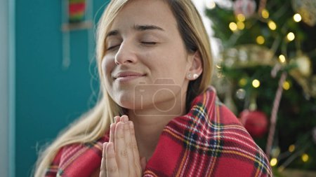 Foto de Mujer rubia joven celebrando la Navidad rezando en casa - Imagen libre de derechos