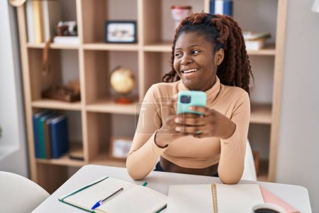 Photo for African american woman student using smartphone sitting on table at home - Royalty Free Image