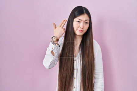 Téléchargez les photos : Jeune femme chinoise debout sur fond rose tirant et se suicidant pointant la main et les doigts vers la tête comme une arme à feu, geste suicidaire. - en image libre de droit