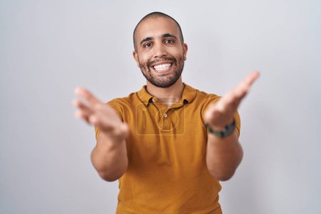 Téléchargez les photos : Homme hispanique avec barbe debout sur fond blanc souriant joyeuse offrant des mains donnant assistance et acceptation. - en image libre de droit