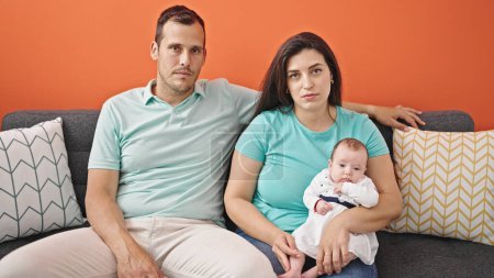 Téléchargez les photos : Famille de trois personnes à l'air sérieux assis sur le canapé à la maison - en image libre de droit