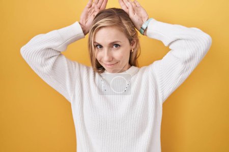 Photo for Young caucasian woman wearing white sweater over yellow background doing bunny ears gesture with hands palms looking cynical and skeptical. easter rabbit concept. - Royalty Free Image