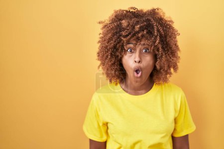 Photo for Young hispanic woman with curly hair standing over yellow background afraid and shocked with surprise expression, fear and excited face. - Royalty Free Image