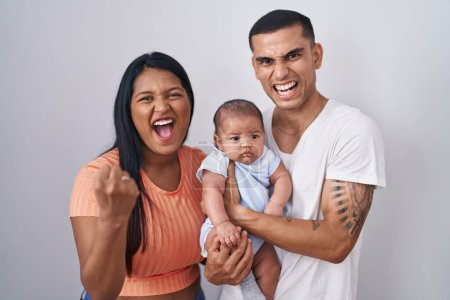 Photo for Young hispanic couple with baby standing together over isolated background angry and mad raising fist frustrated and furious while shouting with anger. rage and aggressive concept. - Royalty Free Image