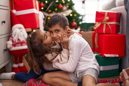 Photo for Brother and sister kissing and hugging each other sitting on floor by christmas gifts at home - Royalty Free Image