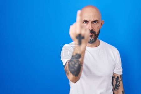 Téléchargez les photos : Hispanic man with tattoos standing over blue background showing middle finger, impolite and rude fuck off expression - en image libre de droit