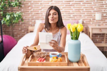 Photo for Brunette young woman eating breakfast in the bed reading a letter looking at the camera blowing a kiss being lovely and sexy. love expression. - Royalty Free Image