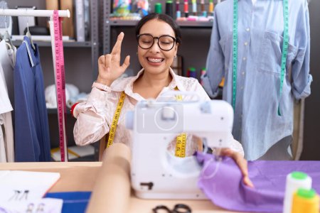 Photo for Young arab woman dressmaker designer working at atelier gesturing finger crossed smiling with hope and eyes closed. luck and superstitious concept. - Royalty Free Image