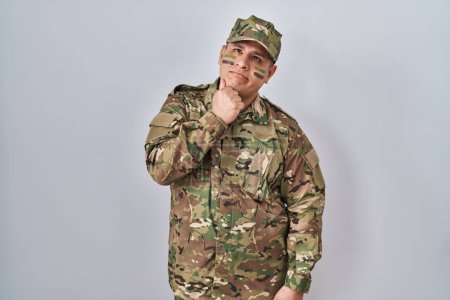 Téléchargez les photos : Jeune homme hispanique portant l'uniforme de l'armée de camouflage avec la main sur le menton penser à la question, expression coûteuse. souriant avec un visage réfléchi. concept de doute. - en image libre de droit