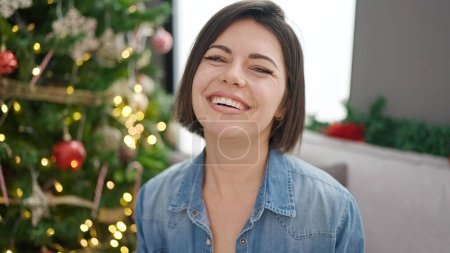 Foto de Joven mujer caucásica sonriendo sentada junto al árbol de Navidad en casa - Imagen libre de derechos