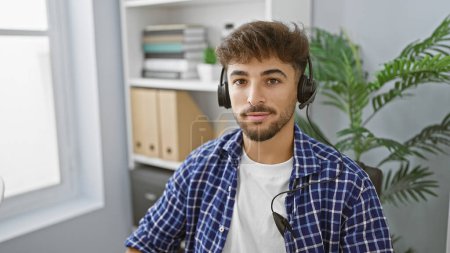 Photo for Handsome young arab man, a successful worker, concentrating on his job, wearing a headset indoors at the office. a professional with a relaxed demeanour, providing aid and service for customers. - Royalty Free Image