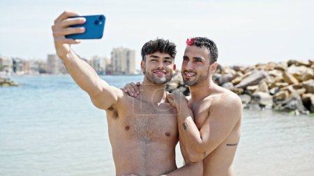 Foto de Dos hombres turista pareja sonriendo confiado hacer selfie por teléfono inteligente en la playa - Imagen libre de derechos
