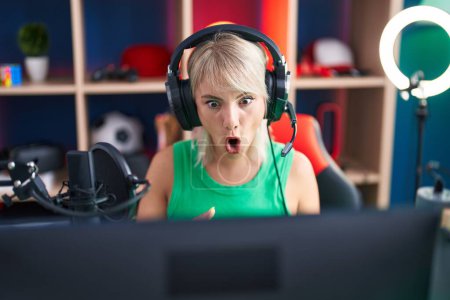 Photo for Young caucasian woman playing video games wearing headphones scared and amazed with open mouth for surprise, disbelief face - Royalty Free Image