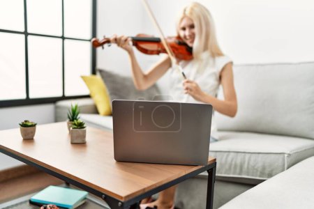 Photo for Young blonde woman musician smiling confident having online violin lesson at home - Royalty Free Image