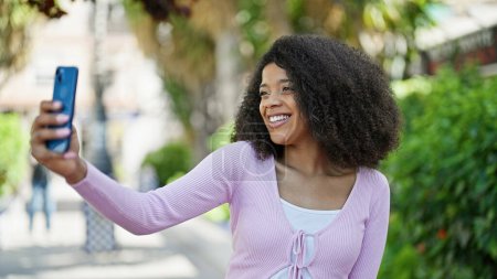 Foto de Mujer afroamericana sonriendo confiada haciendo selfie por el teléfono inteligente en el parque - Imagen libre de derechos
