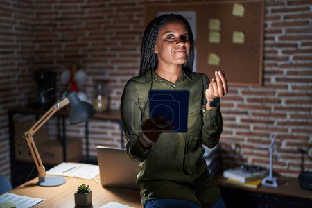 Téléchargez les photos : Jeune afro-américain avec des tresses travaillant au bureau la nuit faire un geste d'argent avec les mains, demander le paiement du salaire, millionnaire entreprise - en image libre de droit