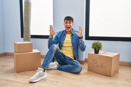 Photo for Young hispanic man sitting on the floor at new home celebrating crazy and amazed for success with arms raised and open eyes screaming excited. winner concept - Royalty Free Image