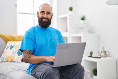 Téléchargez les photos : Jeune homme chauve utilisant un ordinateur portable assis sur la table à la maison - en image libre de droit