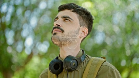 Téléchargez les photos : Jeune homme hispanique touriste portant sac à dos et écouteurs au parc - en image libre de droit
