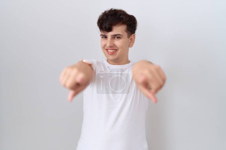 Foto de Joven hombre no binario vistiendo casual camiseta blanca que apunta a usted y la cámara con los dedos, sonriendo positivo y alegre - Imagen libre de derechos