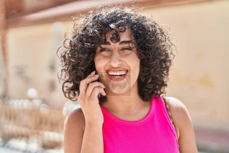Téléchargez les photos : Jeune femme du Moyen-Orient souriant confiant parler sur le smartphone à la salle de jeux - en image libre de droit