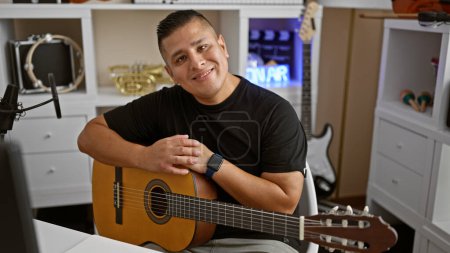Photo for Handsome young latin man, a confident musician, holding his classic guitar and smiling radiantly in a music studio, evoking the melody of his acoustic performance - Royalty Free Image