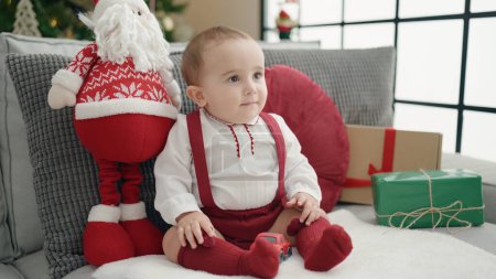 Photo for Adorable hispanic baby smiling confident sitting on sofa by christmas tree at home - Royalty Free Image