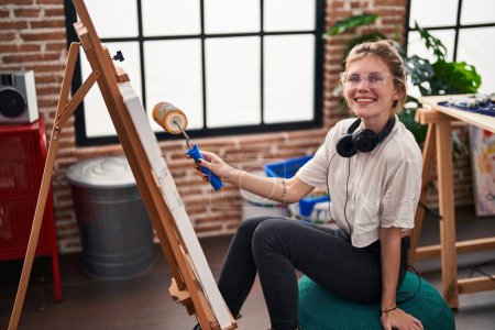 Foto de Joven mujer rubia artista dibujo con pintura de rodillos en el estudio de arte - Imagen libre de derechos