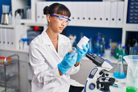 Photo for Young beautiful hispanic woman scientist smiling confident holding pills bottle at laboratory - Royalty Free Image