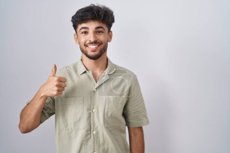 Photo for Arab man with beard standing over white background doing happy thumbs up gesture with hand. approving expression looking at the camera showing success. - Royalty Free Image