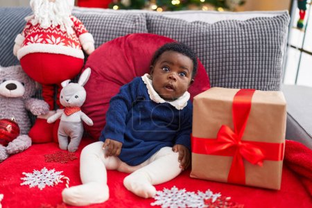 Foto de Bebé afroamericano sentado en un sofá con decoración navideña en casa - Imagen libre de derechos