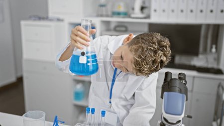 Photo for Adorable blond boy scientist, engrossed in crucial medical research, looking at test tube measurement indoors at a professional lab - Royalty Free Image